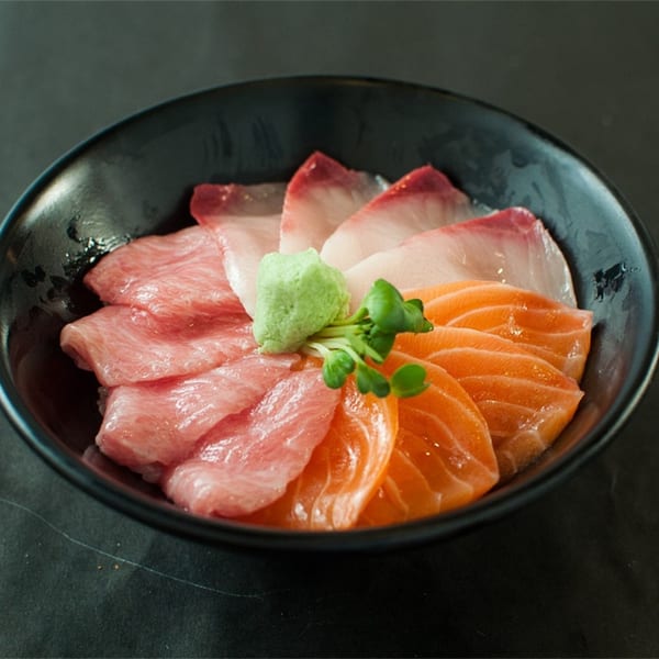 A black bowl of Koi Sushi's sashimi, featuring tuna, salmon, and white fish with wasabi.