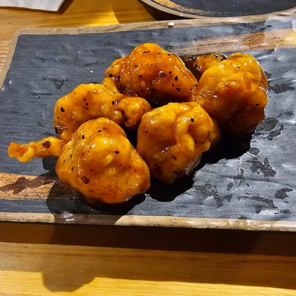 Golden-brown fried chicken pieces coated in a glossy sauce with black specks, served on a dark plate.