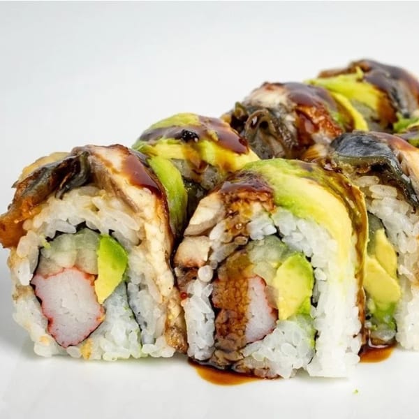 Close-up of Koi Sushi's dragon roll with eel, avocado, and sauce on a white plate.