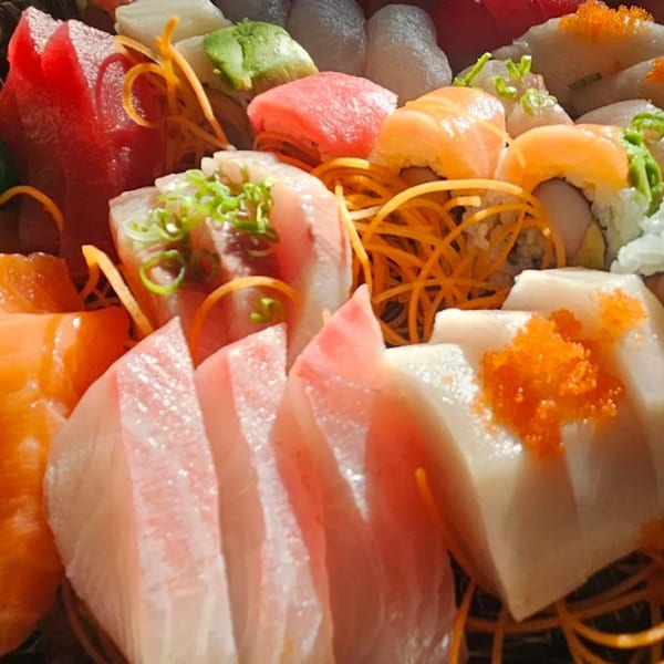 A vibrant platter of Koi Sushi's fresh sashimi and sushi rolls, garnished with shredded carrots and scallions.
