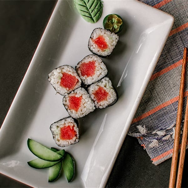 Six pieces of Koi Sushi tuna maki rolls with cucumber, wasabi, and chopsticks on a white plate.