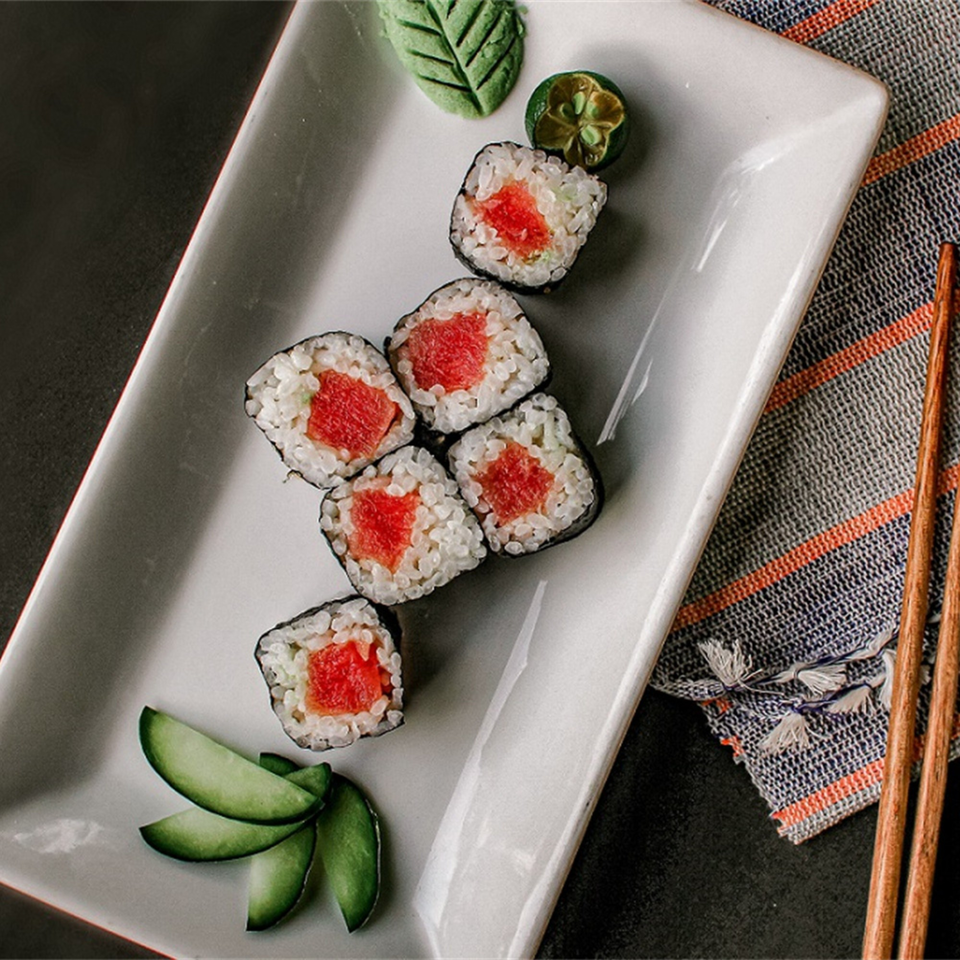 Six pieces of Koi Sushi tuna maki rolls with cucumber, wasabi, and chopsticks on a white plate.