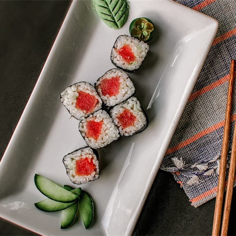 Six pieces of Koi Sushi tuna maki rolls with cucumber, wasabi, and chopsticks on a white plate.
